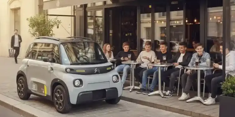 fotografia real del citroen ami electrico aparcado en una calle urbana junto a una terraza con varios jovenes